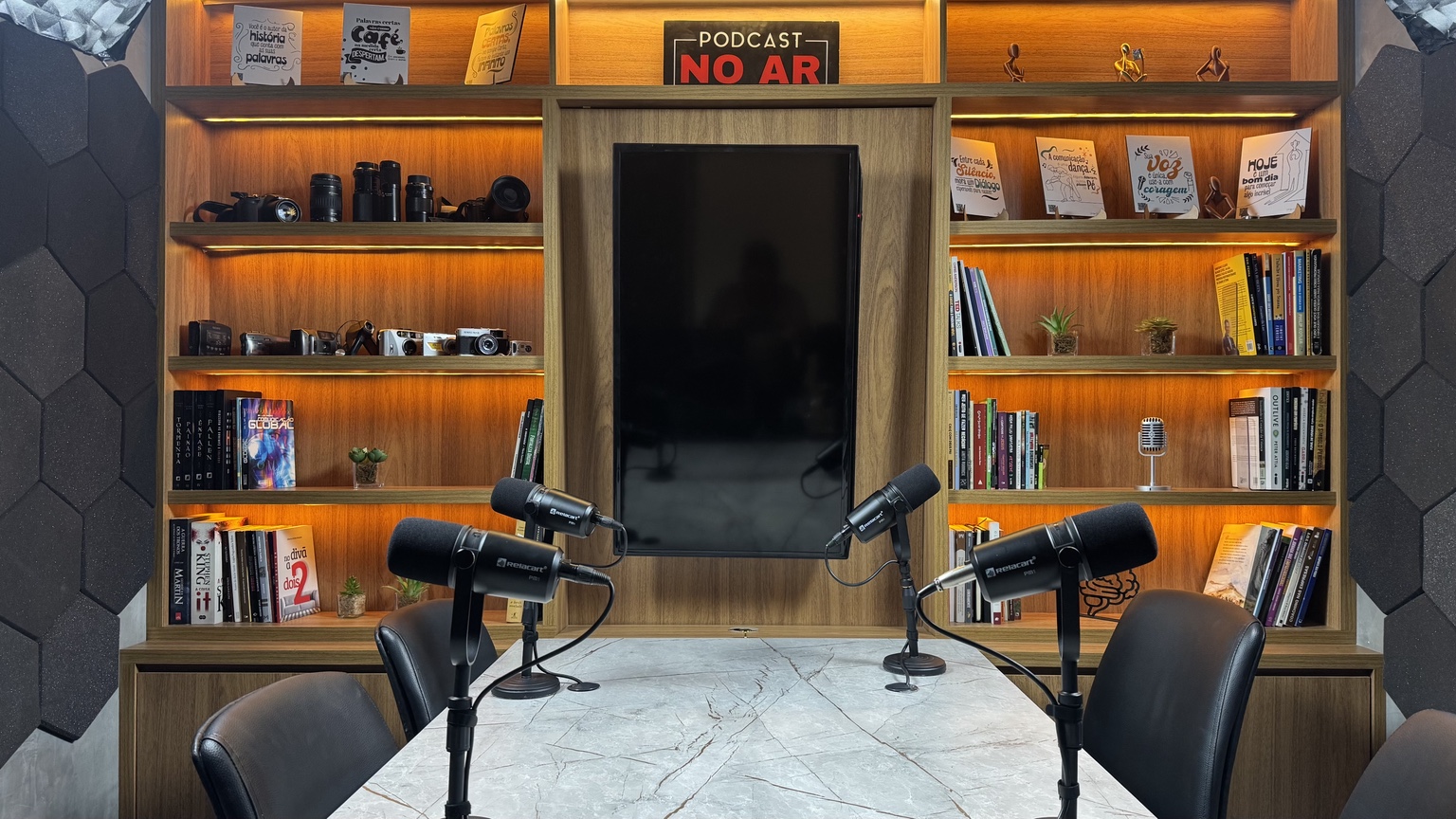 Cenário do Studio V com mesa, quatro microfones e estantes iluminadas